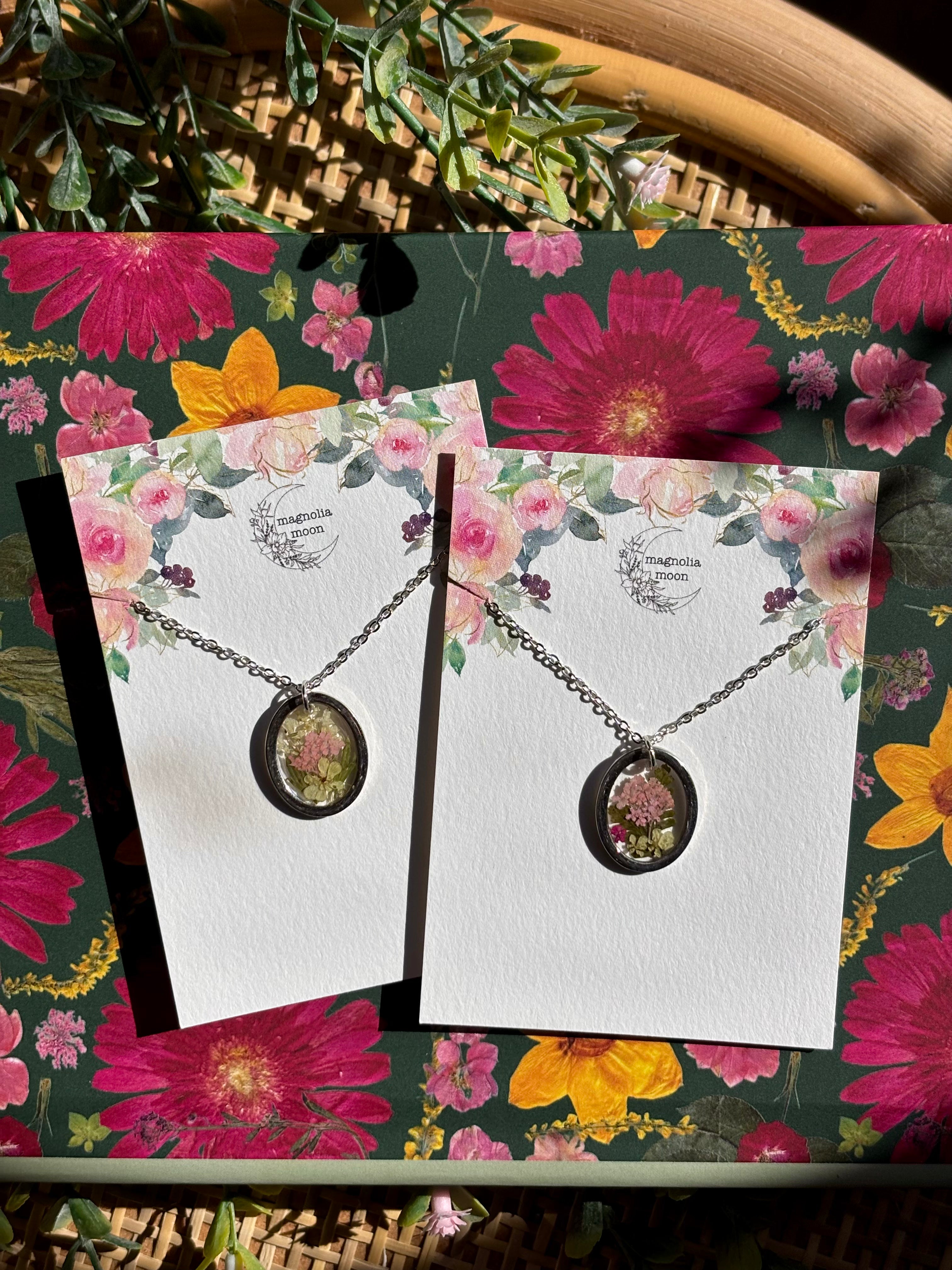 Two necklaces on display cards with a floral background