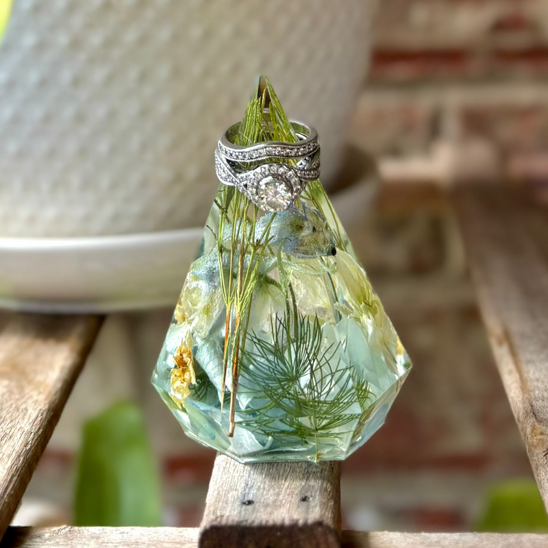 Decorative crystal with a ring on top, placed on a wooden surface with plants in the background.