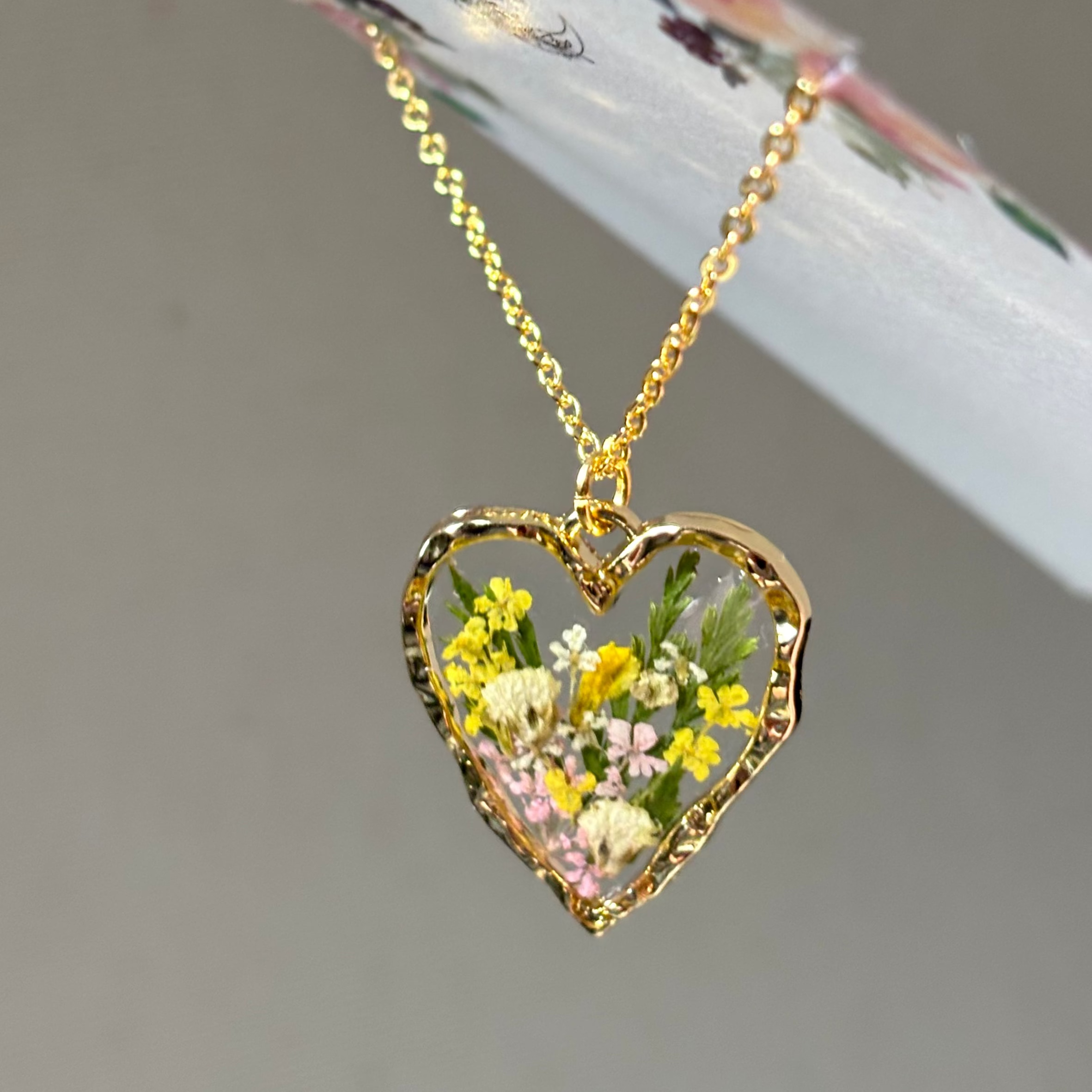 Gold heart-shaped necklace with embedded flowers on a neutral background